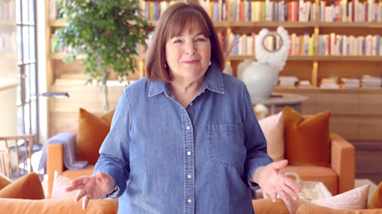 Ina Garten stands in blue shirt in front of bookshelves