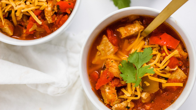 Chicken chili in pot and serving bowls with bowls of fresh cilantro and cheese