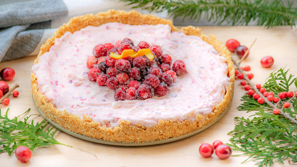 Cranberry orange cheesecake topped with fresh whole cranberries and a spiral of orange peel