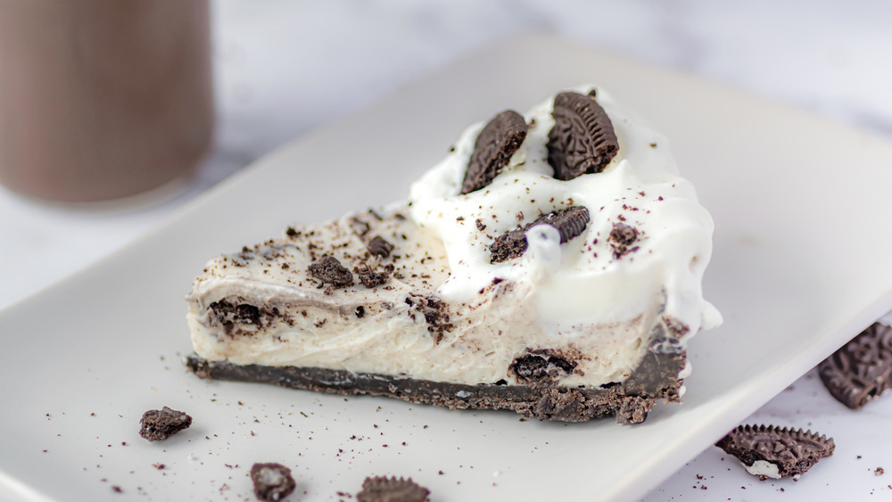 Slice of Oreo cheesecake on a plate with cookie crumbles all around