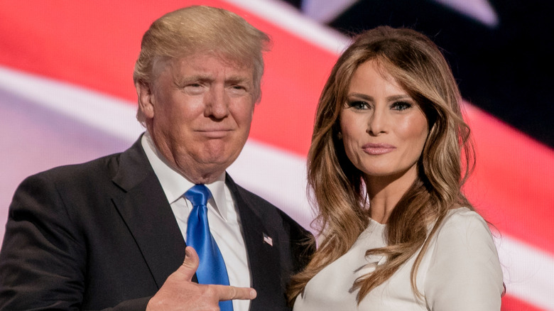 Donald and Melania Trump smiling in front flag background