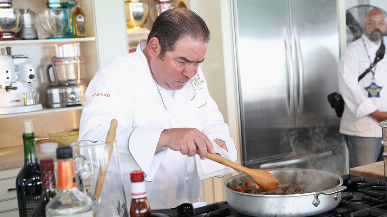 Emeril Lagasse stirring a pot of sauce with serious expression