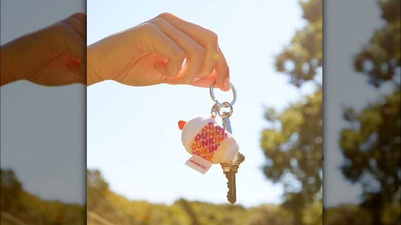 Person holding a key ring with Dunkin's plush iced coffee keychain on it.