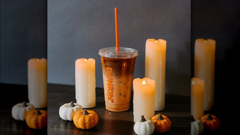 A Peanut Butter Cup iced macchiato from Dunkin' surrounded by candles and pumpkins.