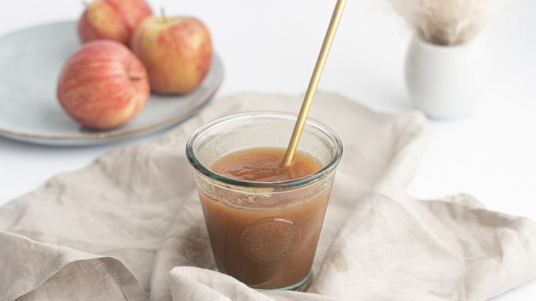 Apple butter in glass cup with apples in background