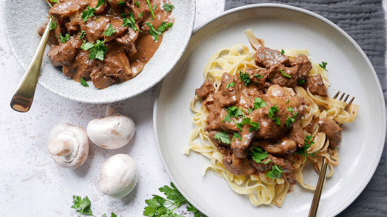 Two plates filled with beef stroganoff, three pieces of mushrooms, and parsley on the table.