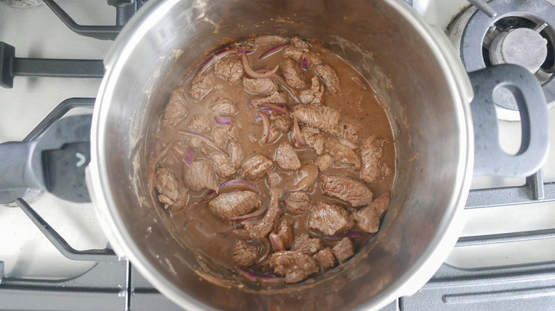 Beef with sauce and sliced onion in a pot.