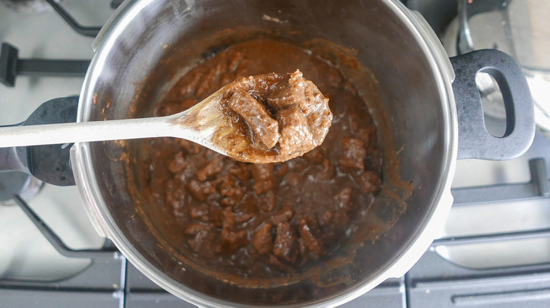 Sliced beef with sauce in a pot and a wooden spoon.