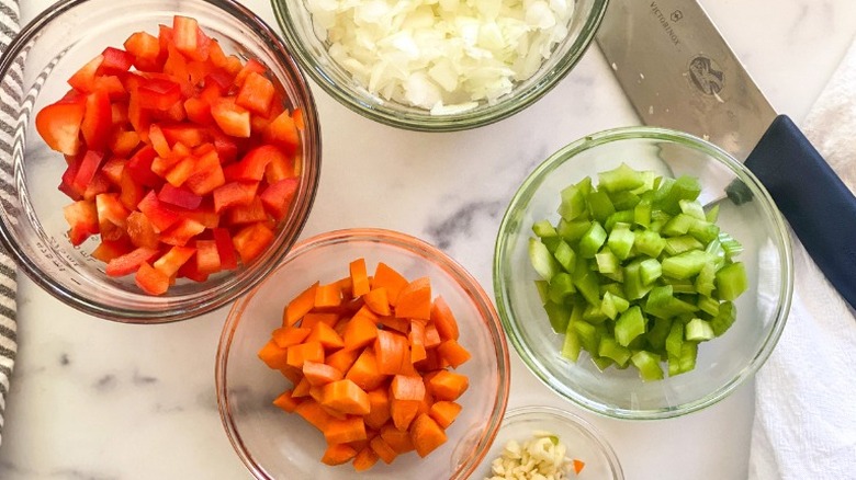 Chopped bell pepper, onion, celery, carrot, and minced garlic in bowls