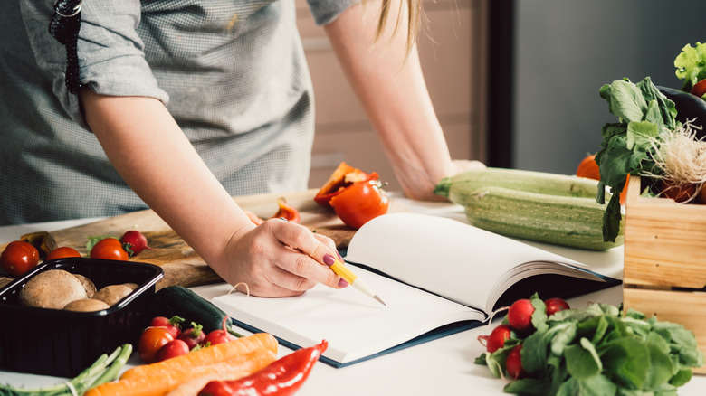 Chef checking recipe on table surrounded by vegetables