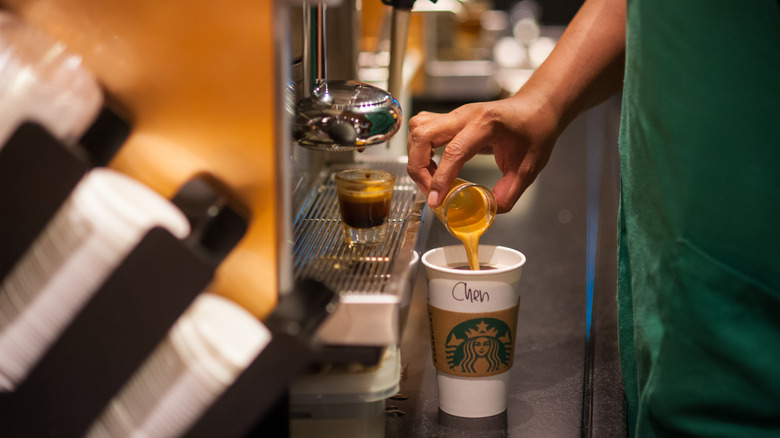 Person pouring espresso shot into a white cup