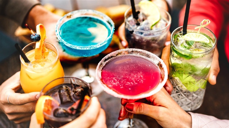 People holding colored drinks together to cheers