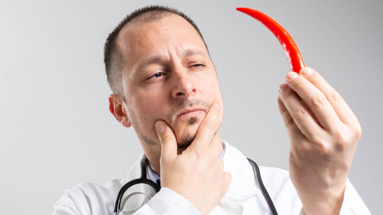 doctor in a white coat holding red hot chili pepper and thinking about Health Benefits of Capsaicin.