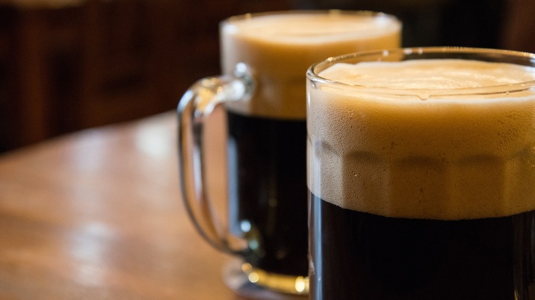 Two foamy dark beer glasses next to each other