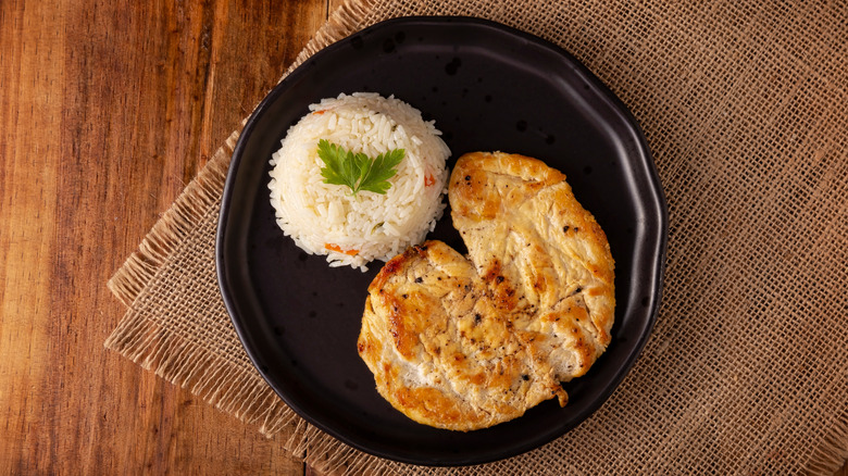 Butterflied chicken breast with rice on black plate