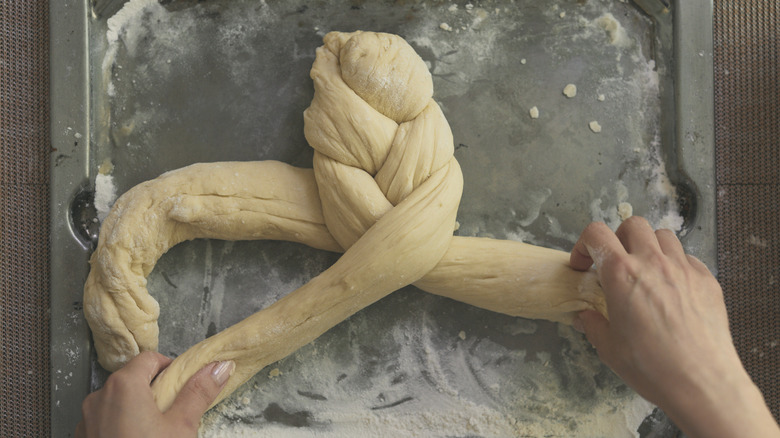 hands braiding challah dough strands on baking sheet