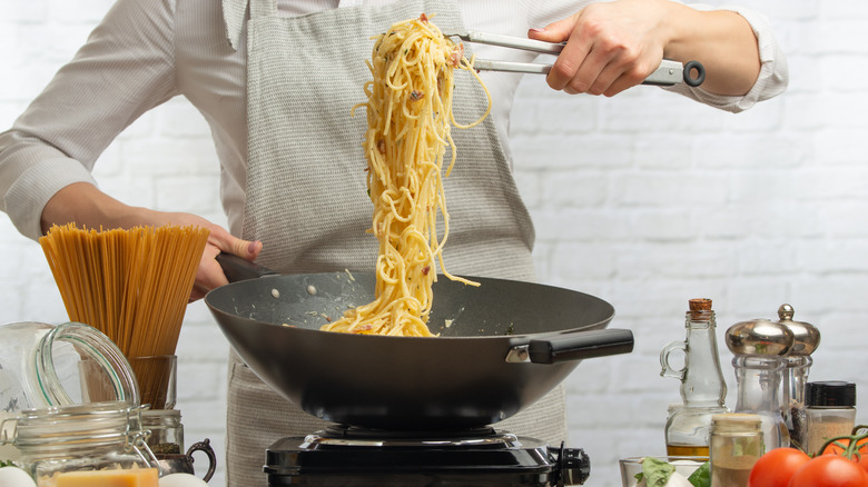 tossing pasta and sauce in pan