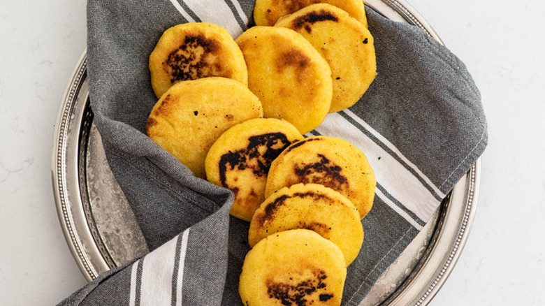Small, griddled corn cakes on a towel-lined plate. 