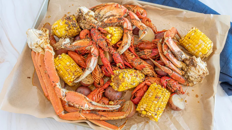 Tray with crab legs, corn, crawfish, and sliced potatoes.