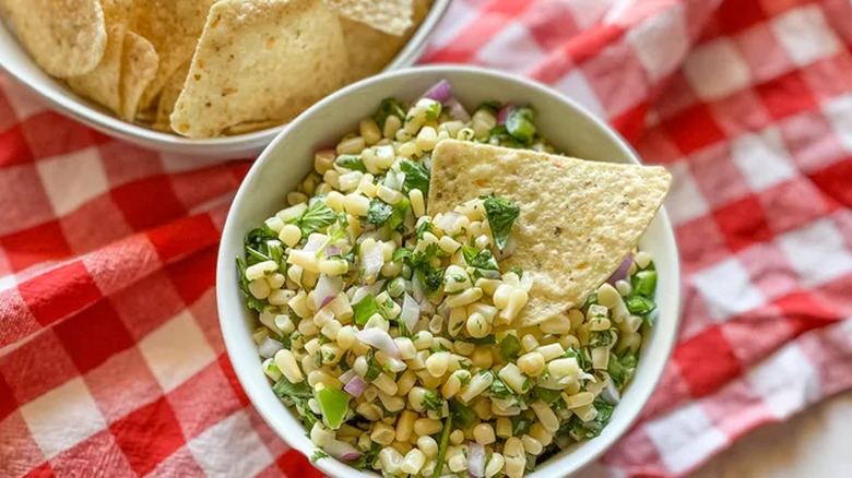 Corn and cilantro salsa in bowl with tortilla chip.