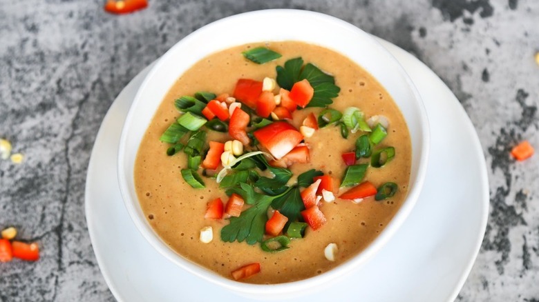 White bowl with thick chowder and fresh veggies on top.