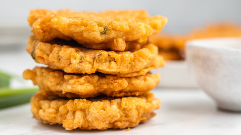 Stack of four, flat, fried corn fritters. 