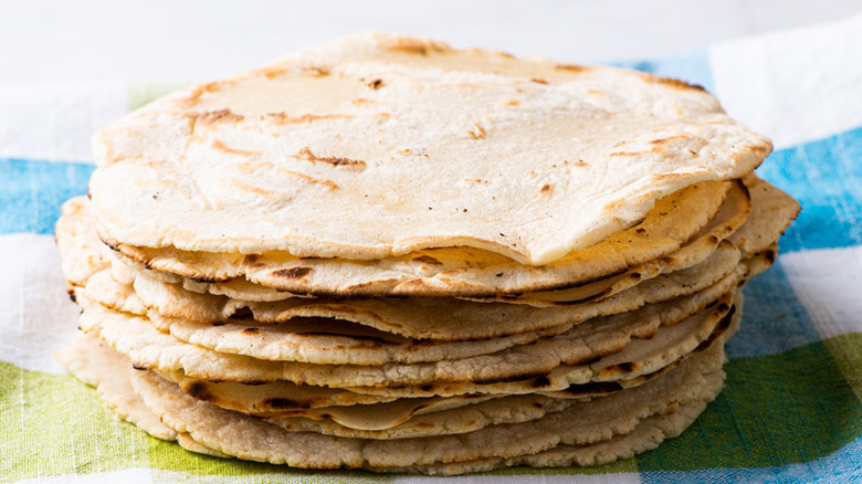 Stack of homemade corn tortillas on striped cloth.