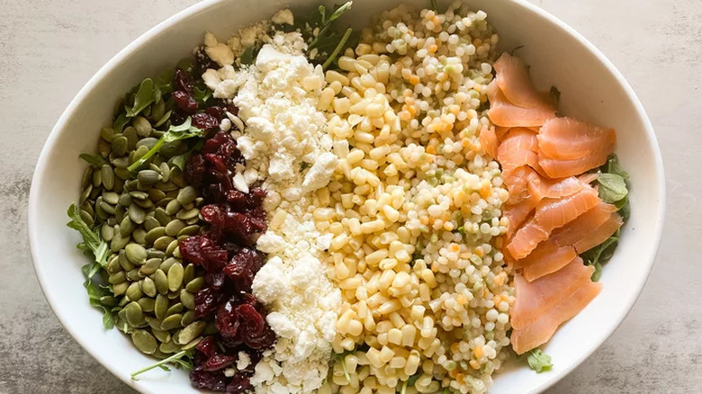 Rows of pepitas, feta cheese, corn, and salmon over salad. 