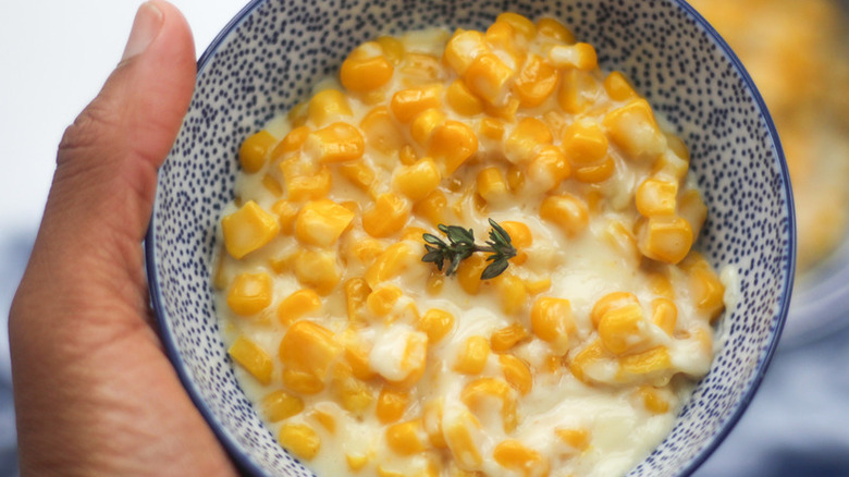 Hand holding small bowl of creamy corn.  