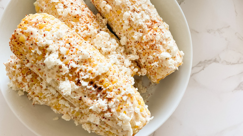 Ears of corn with creamy sauce and cheese crumbles.