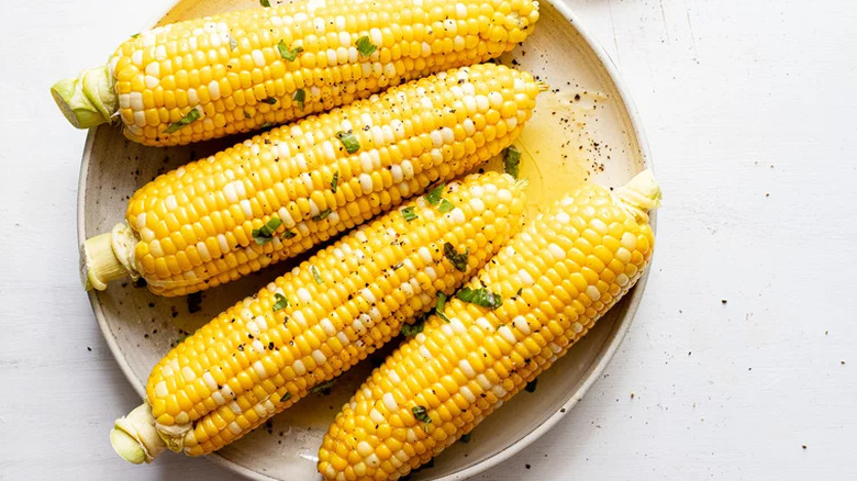 Four ears of cooked corn on plate with black pepper. 