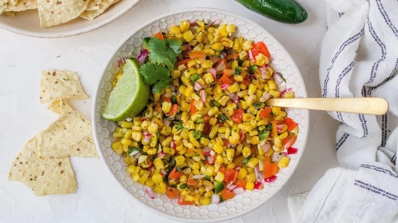 Bowl of corn salsa with chips and lime wedge.