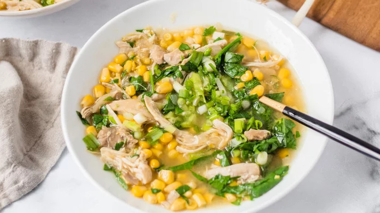 Soup with corn, chicken, and greens in white bowl. 