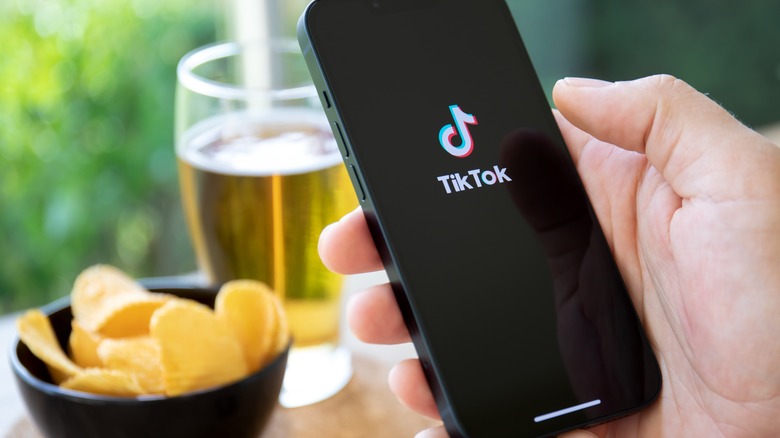 Hand holding TikTok on phone by food and drink