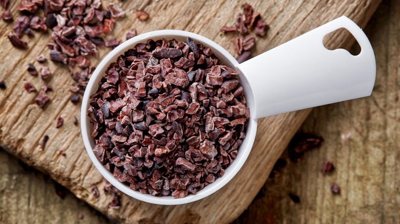 Cup of cocoa nibs on wooden surface