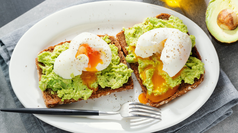 Avocado toast with runny egg on a white plate