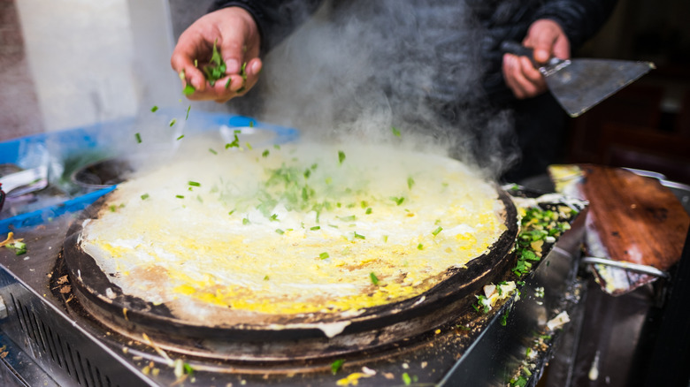 vendor sprinkling scallions onto jianbing