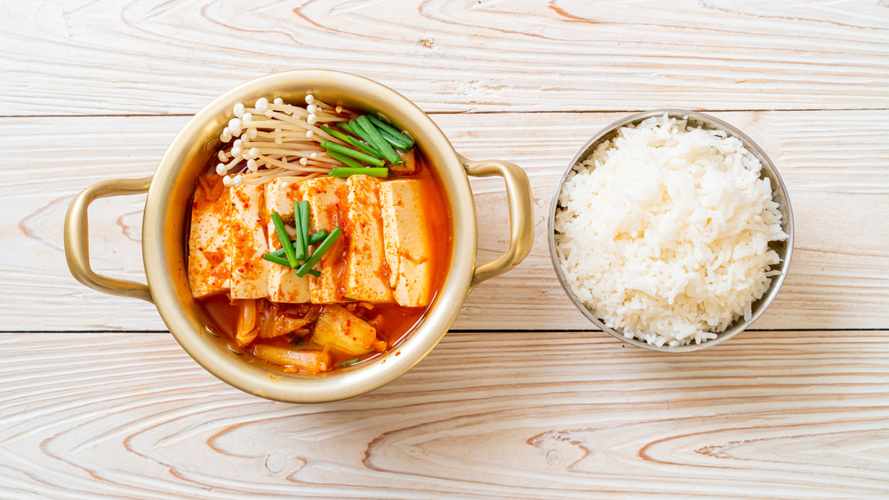 A bowl of kimchi jjigae and a bowl of rice on a light wooden table