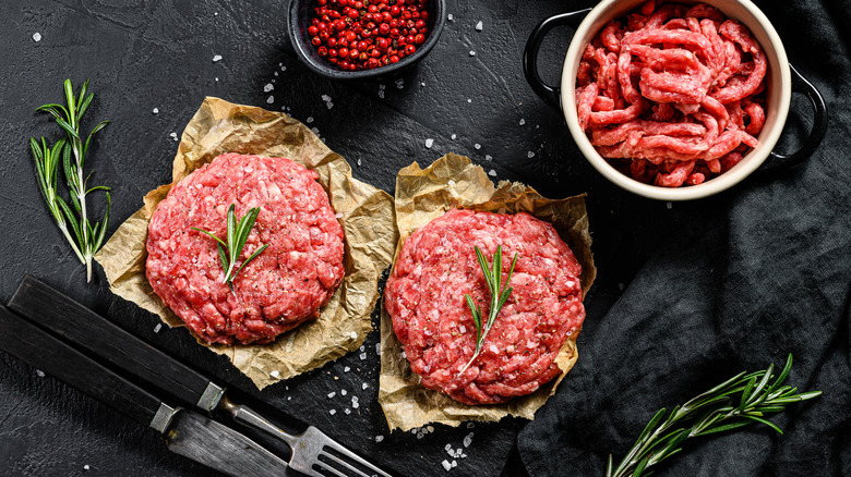 Raw burger patties with seasoning and rosemary sprig