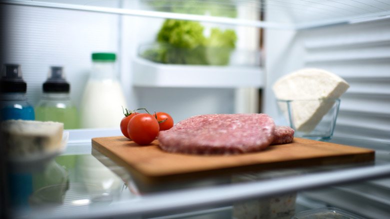 Raw burger patties on cutting board in fridge