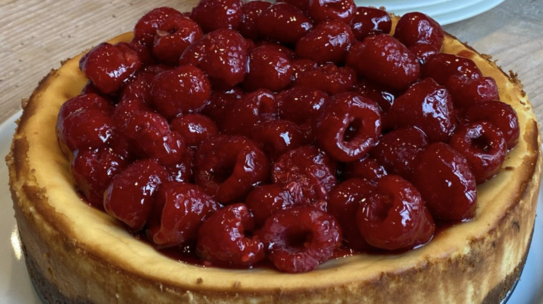 Whole cheesecake topped with syrupy raspberries