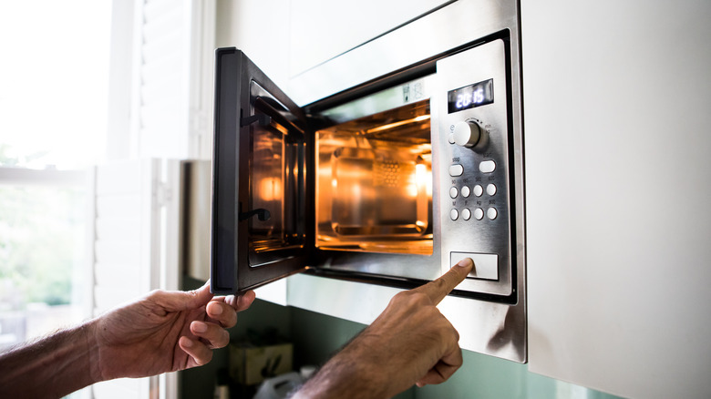 A person's hands operate a microwave.