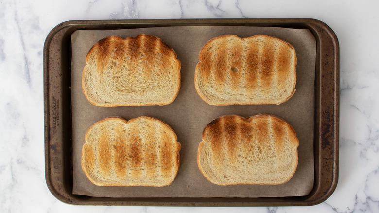 Four slices of toasted bread on baking sheet