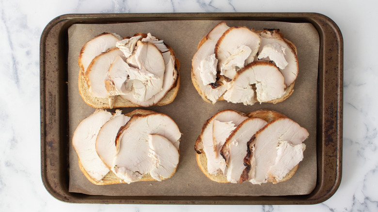 Turkey slices on four pieces of bread on baking sheet