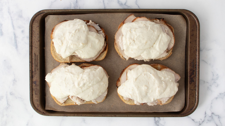 Four open-faced sauce covered sandwiches on baking sheet