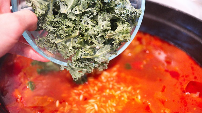 pouring kale into tomato stew