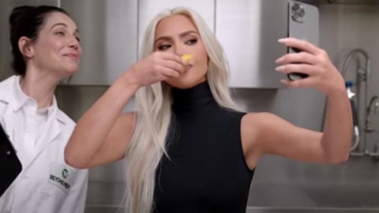 Kim Kardashian holding food in front of her face while taking a selfie