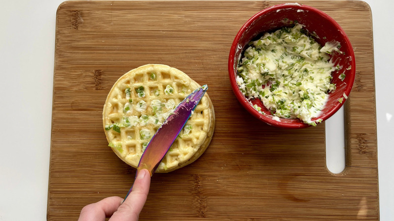 Knife spreading scallion butter onto waffle