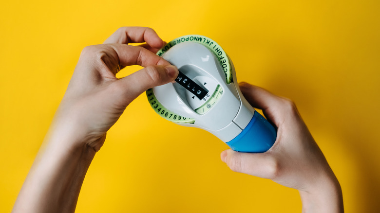 Hand holding a label maker against a yellow background