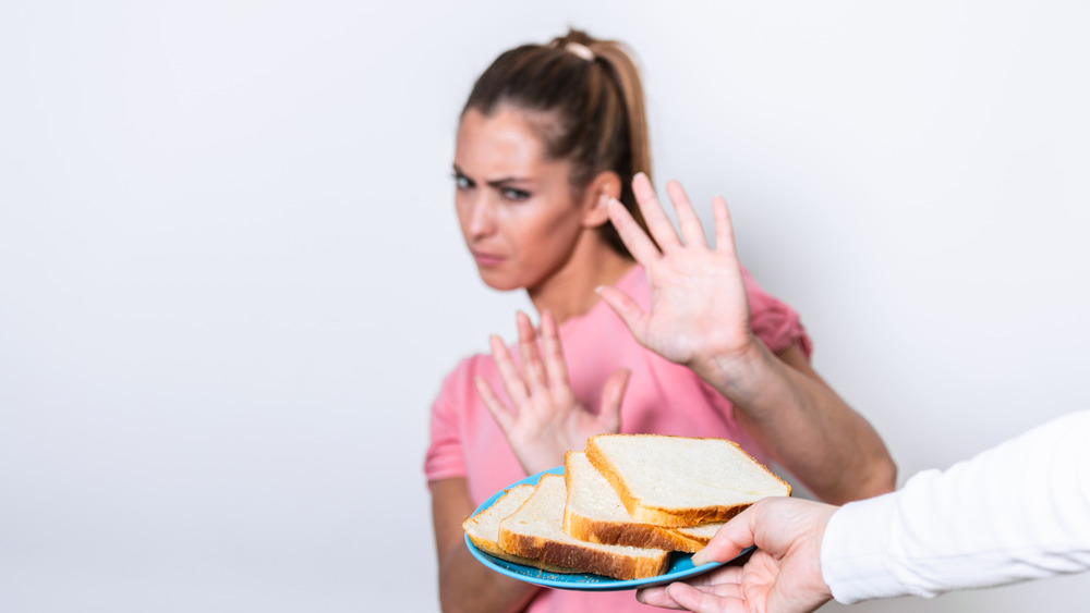 A woman refuses a platter of sliced bread in an attempt to stave off gluten. However, the real issue here is the question of why would someone offer a person a platter of sliced white bread? Nothing's on it. It isn't even special bread. No wonder the refusing person looks so concerned.